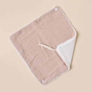 Detail of soft cotton muslin baby bib with pom-pom trim and snap button closure