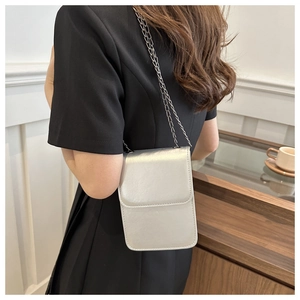 Silver metallic chain phone bag shown on shoulder with minimalist black dress style