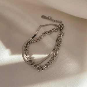 Detailed view of layered silver Cuban and snake chain bracelet on textured fabric