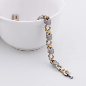 Dettaglio del bracciale a maglie a cuore bicolore oro e argento su una ciotola bianca