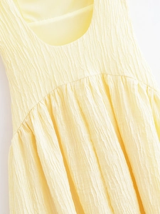 Detailed close-up of light yellow plissé fabric texture and delicate pleated neckline detail