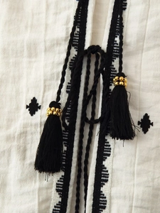 Detailed close-up of geometric embroidery and black tassels with gold beads on cotton fabric