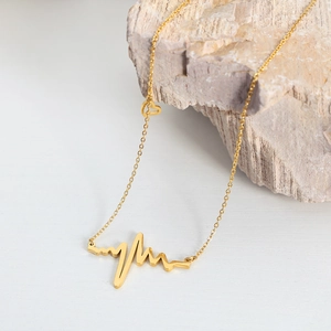 Minimalist gold heartbeat pendant necklace on stone background with small heart detail