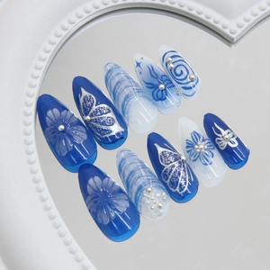 Blue and white stiletto press-on nails with 3D floral and butterfly art on a mirror