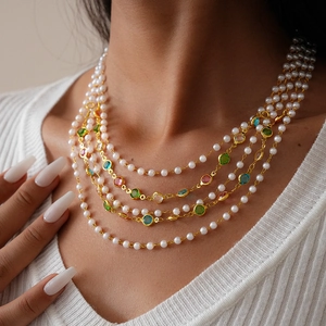 Detail of layered gold necklace featuring multi-colored gemstones and pearls on white sweater