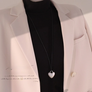 Minimalist silver heart pendant necklace on black cord worn over an elegant beige blazer