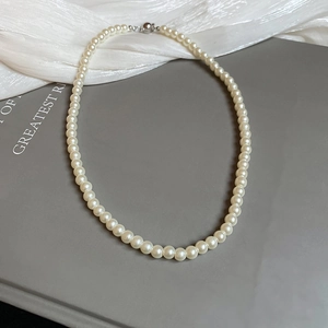 Detailed close-up of a classic white pearl necklace with a silver clasp on silk fabric