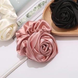 Macro detail of satin rose hair scrunchies in pink, black and white on a wooden tray