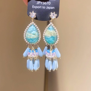 Macro detail of teardrop resin earrings with white pearls and blue bead tassels