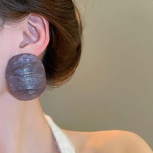 Macro detail of oversized round resin earrings with brushed dark purple texture