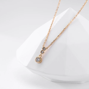 Detail of gold necklace featuring three graduated round cubic zirconia stones on white prop