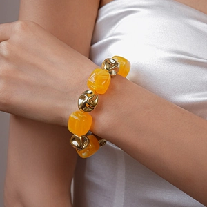 Detail of yellow acrylic square beads and golden irregular beads on a woman's wrist
