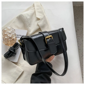 Detail of black faux leather bag featuring glossy finish and elegant gold hardware clasp
