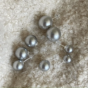 Detailed view of grey faux pearl stud earrings in various sizes on soft fabric
