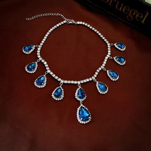 Dettaglio di una collana in argento con gemme blu a goccia e cristalli su sfondo rosso