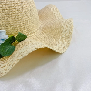 Detail of woven straw sun hat brim featuring blue floral decor and wavy edge design