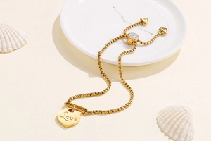 Detail of adjustable gold heart bracelet with Love engraving and seashell background