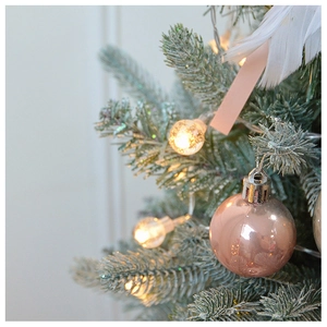 Close-up of pink shiny baubles and warm LED globe lights on a snow-flocked Christmas tree