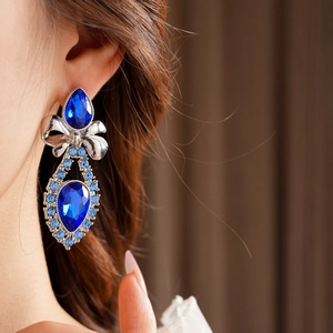 Close-up of vintage silver bow earrings with teardrop blue crystal pendant on a model