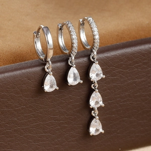 Close-up of three silver water drop earrings with clear zircon stones on soft suede