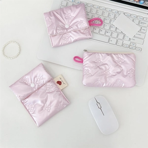 Close-up of pink quilted satin cosmetic bags with bow embroidery on a white desktop