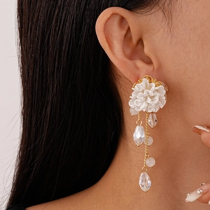 Close-up of white fabric flower earrings with golden tassels and crystal beads on a model