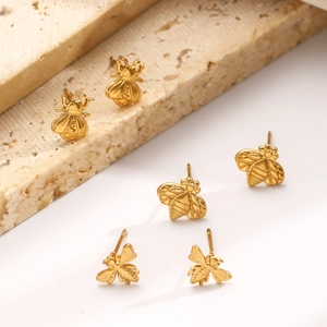 Detailed view of three gold bee-shaped stud earrings on a textured stone surface