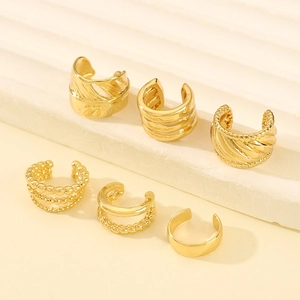 Set of six vintage gold ear cuffs with textured patterns on a white minimalist pedestal