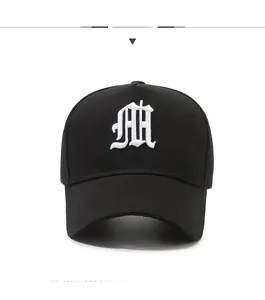 Detailed close-up of white gothic letter M embroidery on a black cotton baseball cap