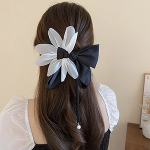 Detail of elegant black satin bow hair clip with white chiffon petals and pearl pendant