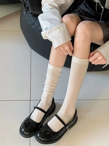 Detail von cremeweißen Netz-Socken mit schwarzen Mary Janes und Schulrock im JK-Stil