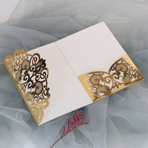 Detail of white laser-cut wedding invitation with elegant gold floral patterns on gauze