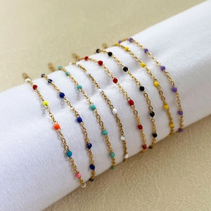 Golden minimalist chain bracelet with colorful enamel beads on a white display roll