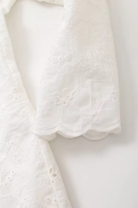 Close-up of white hollow embroidery and delicate scalloped edges on the blazer sleeve
