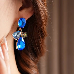 Close-up of vintage gold earrings with blue rhinestones and iridescent gems on model