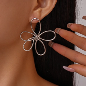 Close-up of polished silver flower hollow wire earrings worn on model's ear