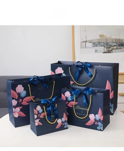 Detail of four navy floral paper gift bags with golden rope handles and blue bows