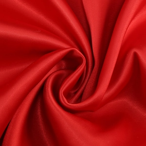 Detail of red satin fabric showing silky texture and pleated spiral folds for elegant dress