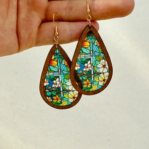 Detail of teardrop wooden earrings with colorful church glass patterns held by hand