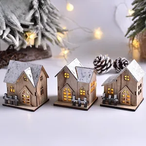 Close-up of three lighted wooden Christmas houses with snowy roofs on a festive desk