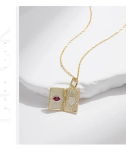 Detail view of a gold locket necklace featuring a red stone and engraved heart motif
