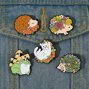 Set of five cartoon enamel pins featuring hedgehogs, frogs, and cats on denim fabric