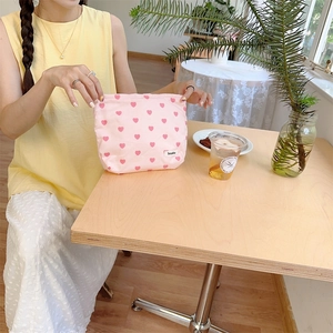 Close-up of pink canvas bag with heart pattern and brand tag on a wooden table