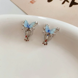 Macro detail of 18k gold plated butterfly ear clips with zircons and blue resin wings