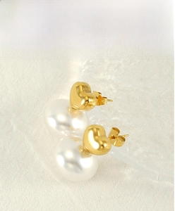 Detail view of heart-shaped gold studs with large white pearls on a textured background