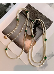 Detailed view of luxury pearl necklace with green gemstone beads on a marble background