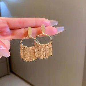 Hand-held shot of gold plated oval fringe earrings with sparkling metallic tassels