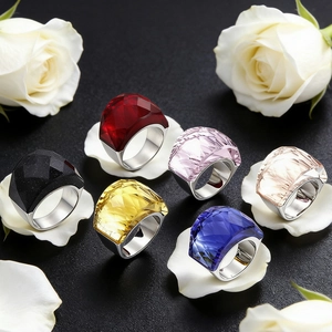 Détail de six bagues cocktail avec cristaux facettés colorés sur un fond texturé noir