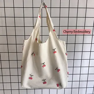 Dettaglio del ricamo di ciliegie rosse su una borsa tote in tela bianca con tessuto materico