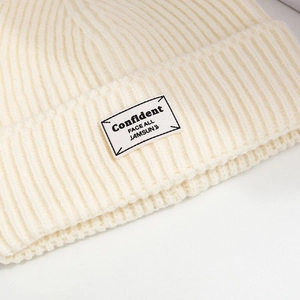 Close-up of beige ribbed knit beanie featuring an embroidered rectangle logo patch